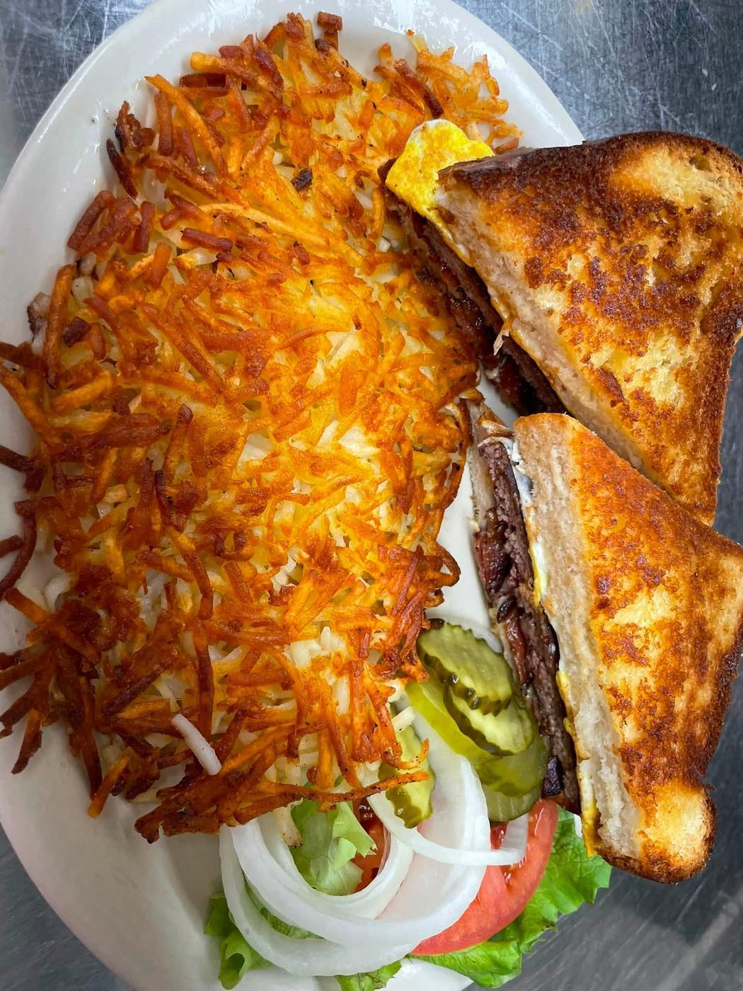 A patty melt on griddled bread cut in half, served with a wide pile of hash browns.